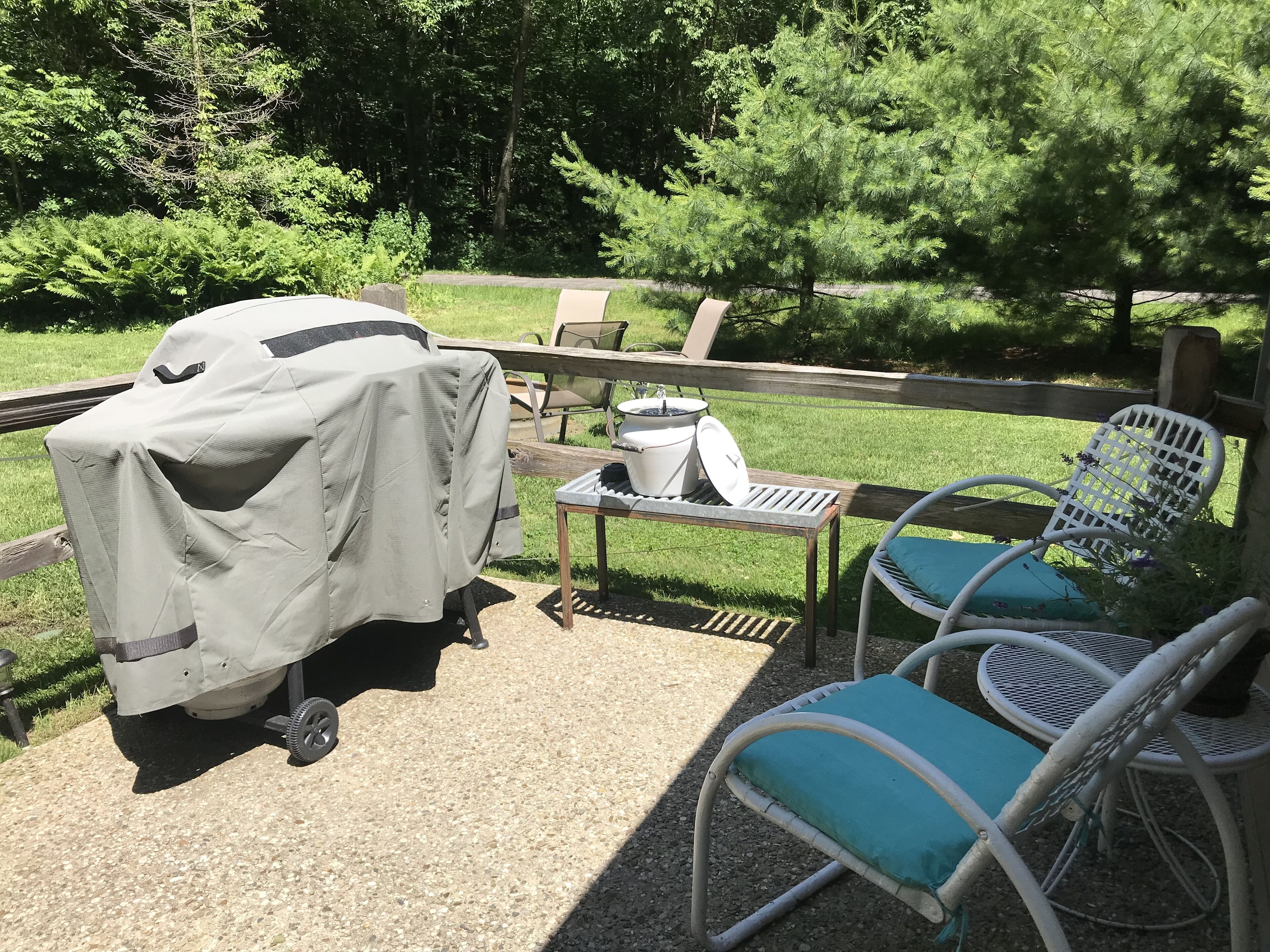 An outdoor patio with a covered grill, a table with a pot, and two chairs.