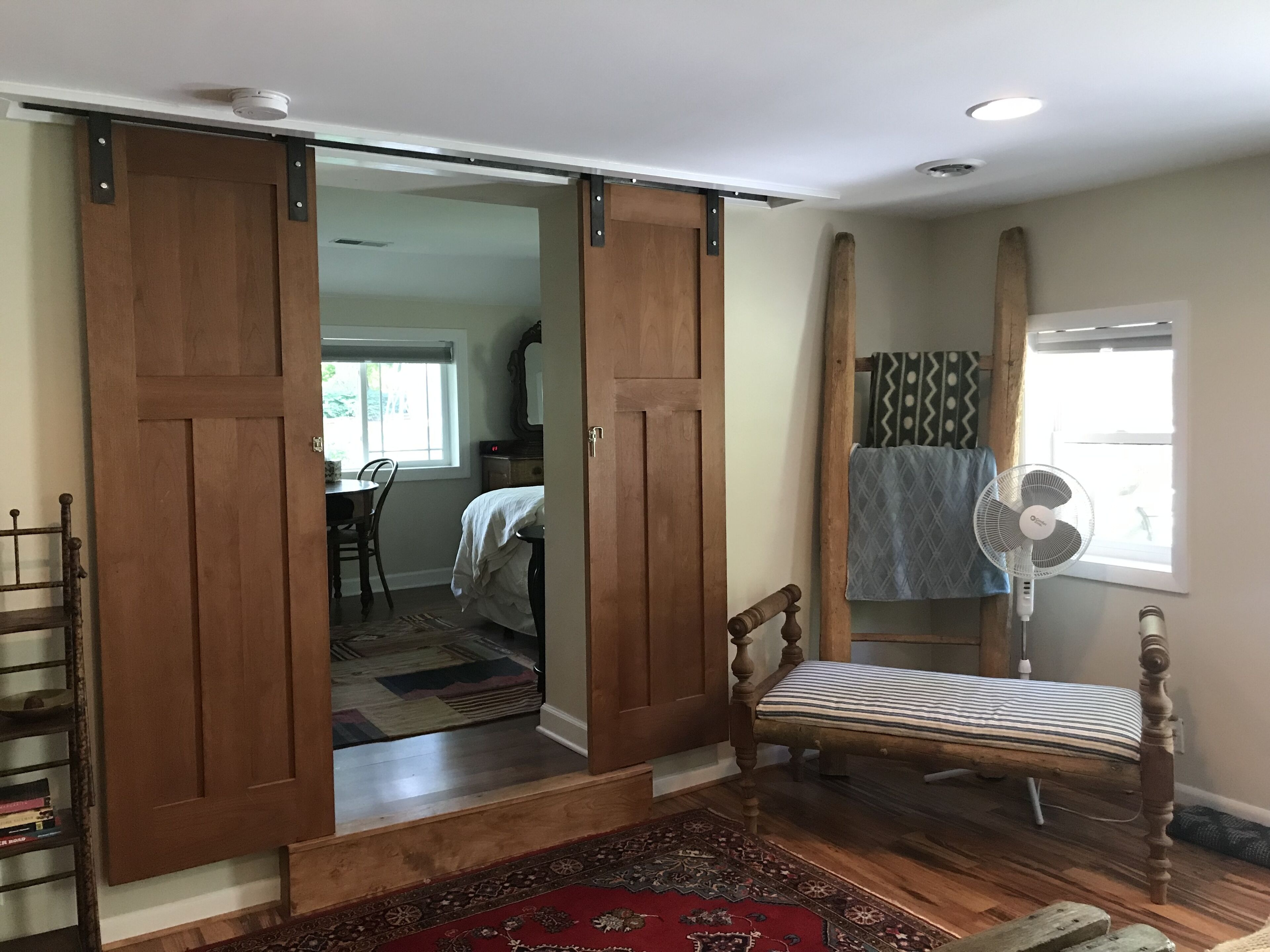 Una habitación con cama, banca, ventilador y puerta corredera.