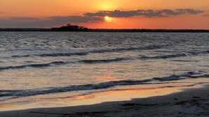 Uma praia ao pôr do sol, com ondas se aproximando da costa.