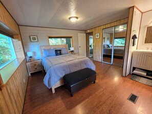 A bedroom with a bed, bedside tables, a bench, a window, and a door leading to another room.