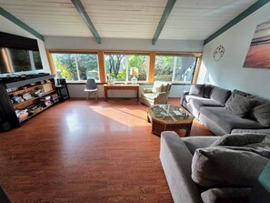 A living room with a sofa, armchair, and coffee table, a bookshelf, and a television.