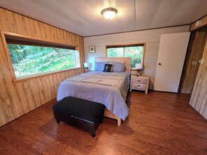 A bedroom with a bed, bedside tables, a bench, and large windows.