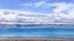 A coastal landscape with clear blue waters, distant mountains, and a partly cloudy sky.
