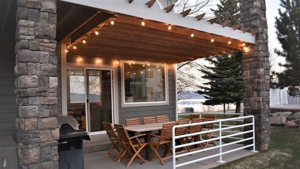 An outdoor patio with a wooden table and chairs, stone pillars, and string lights.