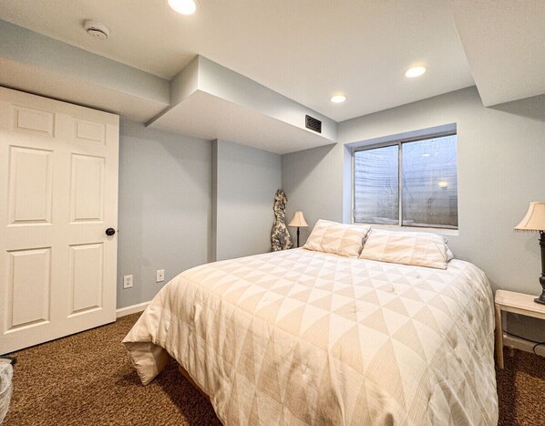 A bedroom with a bed, a window, a door, and a nightstand.
