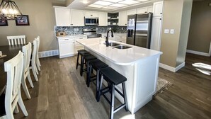 A modern kitchen with white cabinetry, a large island with bar stools, stainless steel appliances, and a pendant light.