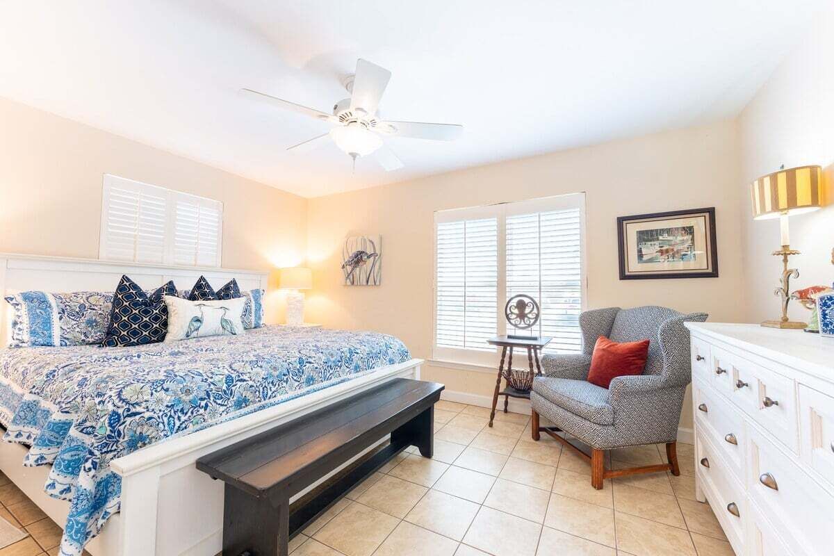 A bedroom with a bed, a chair, a dresser, a ceiling fan, and a window with blinds.