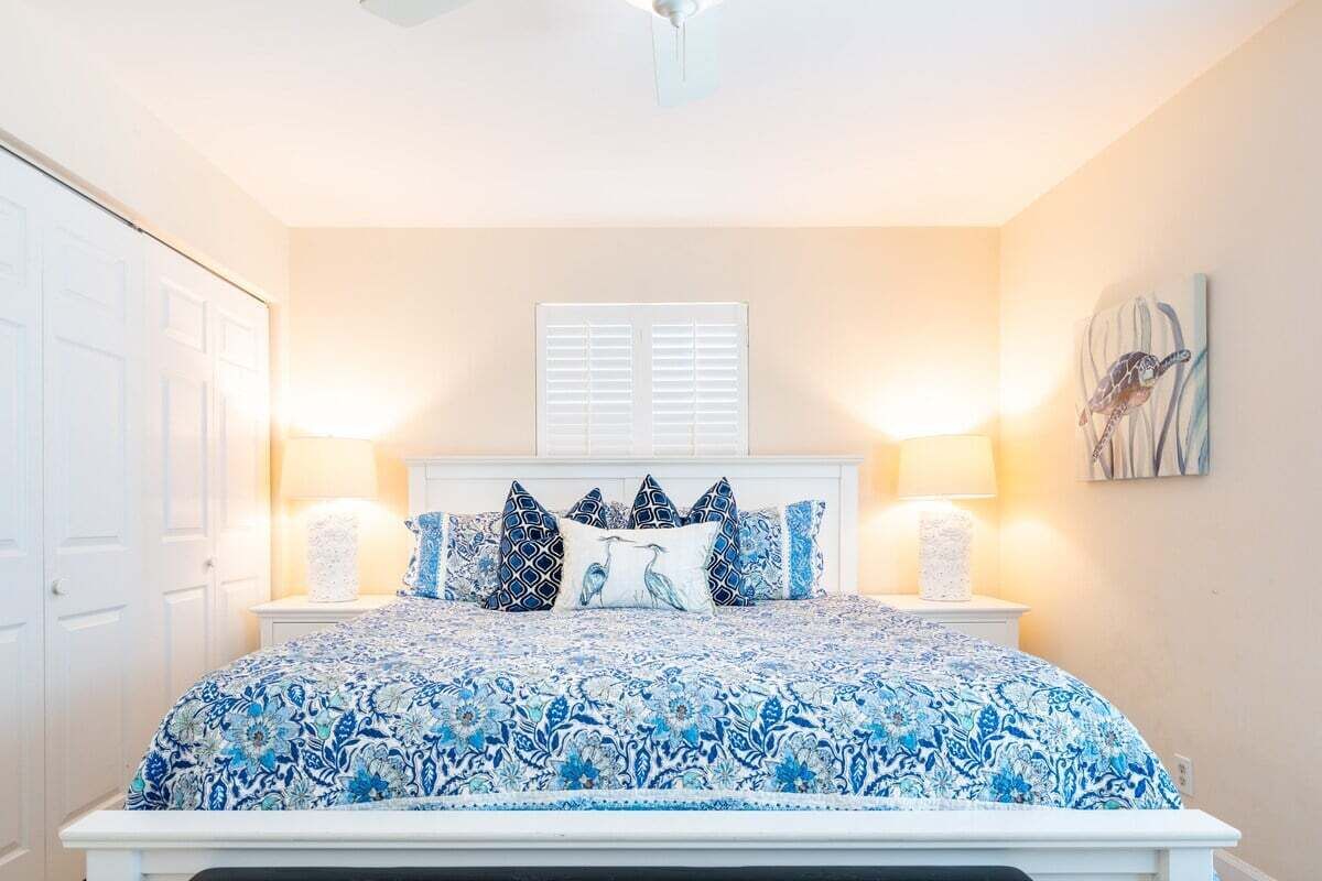 A bedroom with a bed, bedside lamps, a window with shutters, and a painting on the wall.