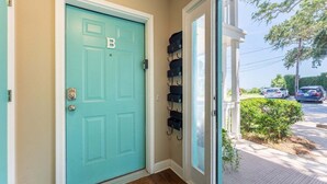 A teal door with a 'B' on it, a set of black storage bins on the wall, and a view of parked cars outside. - Ocean View 2BR Condo Near Pier Village | St. Simons Island Vacation Rental (St Simons Island)