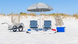 A beach setup with two blue beach chairs, a gray umbrella, a small cart, and a blue cooler. - Ocean View 2BR Condo Near Pier Village | St. Simons Island Vacation Rental (St Simons Island)