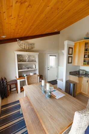 Un espace repas comprenant une table en bois, des chaises, un buffet et un coin cuisine avec des meubles de rangement en bois et un plan de travail.