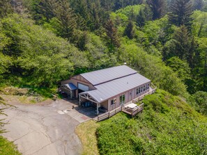 Un edificio de dos pisos con techo metálico, rodeado de un bosque denso.