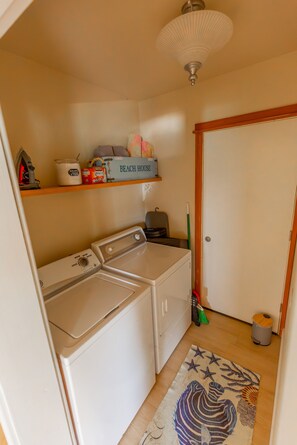 Une buanderie équipée d’un lave-linge, d’un sèche-linge et d’une étagère contenant des produits de nettoyage.