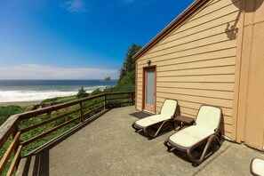 A wooden building with a balcony overlooking the ocean, featuring two lounge chairs and a small table.