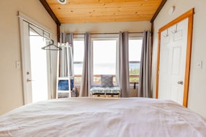 Une chambre à coucher avec un lit, une fenêtre avec des rideaux, un banc avec des coussins et une porte.