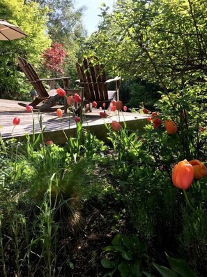 A wooden deck surrounded by lush greenery and red tulips.