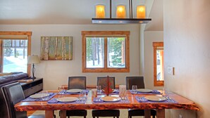 A dining area with a wooden table set for six, surrounded by chairs, with a view of trees through large windows. -  The Perfect Family Mountain Getaway (Breckenridge)