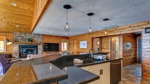 A spacious kitchen with granite countertops, a stone fireplace, wooden walls, and pendant lighting. - Beautiful 7 Bed, 6 Bath, Huge Dock, Boat Launch @ House, Game Room, Kid Friendly (Sunrise Beach)