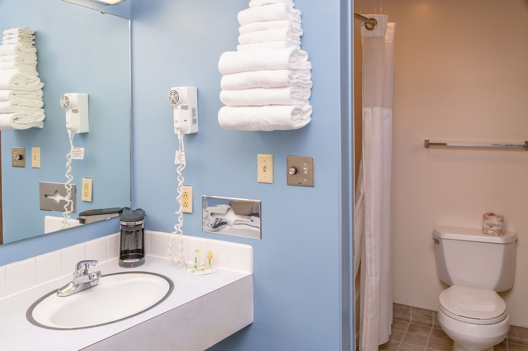 A bathroom with a sink, mirror, towel rack, hair dryer, and toilet.