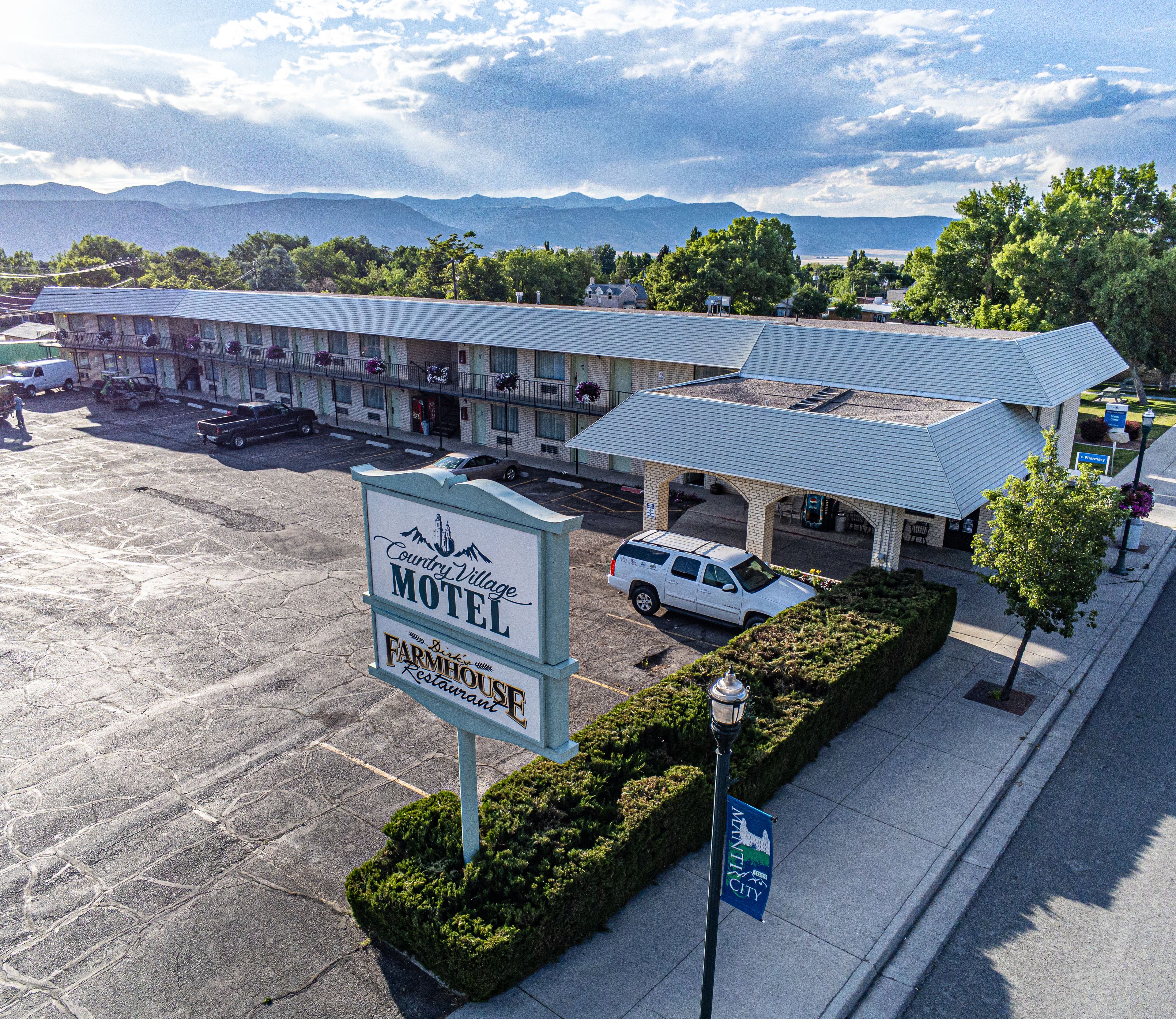 A motel with a Farmhouse Restaurant, a parking lot, and a view of mountains in the background.