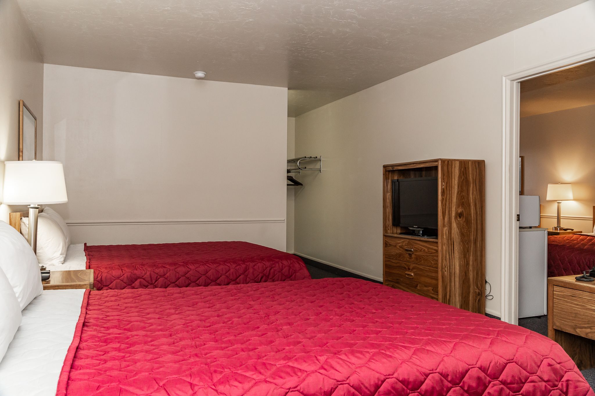 A hotel room with two beds, a wooden wardrobe, a TV, and a desk with a lamp.