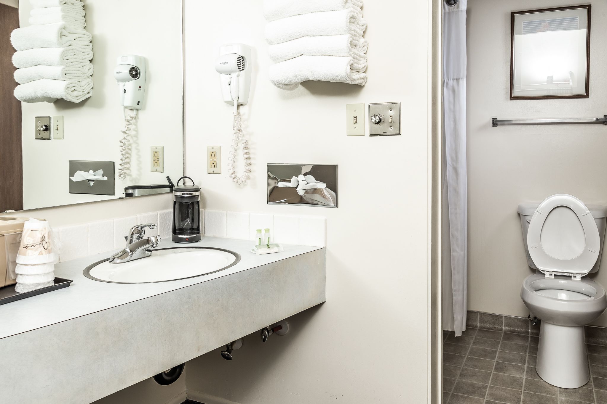 Ein Badezimmer mit Waschbecken, Spiegel, Haartrockner, Handtuchhalter und Toilette.