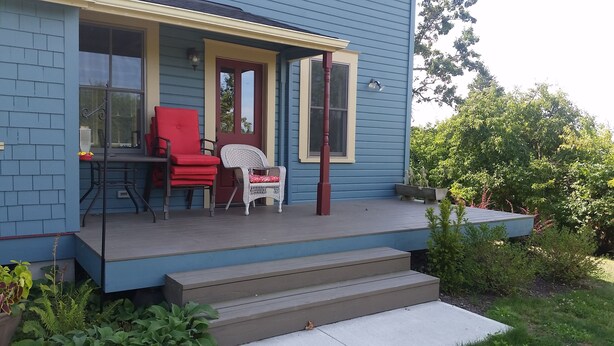 Ein blaues Haus mit Veranda, ein roter Sessel, ein weißer Stuhl und ein kleiner Tisch.