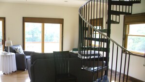 A living room with a wooden floor, a dark-colored sofa, a small table with a lamp, and a spiral staircase with a metal railing. - Garden Cottage near Asheville and Blue Ridge Parkway (Fairview)