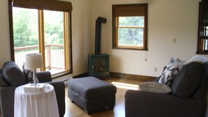 A living room with a fireplace, two sofas, a table, and large windows. - Garden Cottage near Asheville and Blue Ridge Parkway (Fairview)