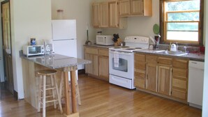 A kitchen with wooden cabinets, a stove, a microwave, and a refrigerator. - Garden Cottage near Asheville and Blue Ridge Parkway (Fairview)
