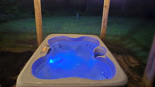 Een hottub onder een houten pergola met lichtslingers, omringd door een gazon.