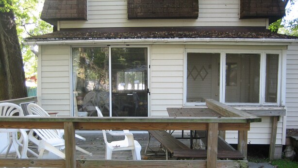 A covered deck with outdoor furniture and a sliding glass door leading to a covered patio area. - Bemus Point Vacation Rental (Bemus Point)