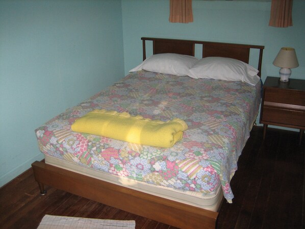 A bed with a floral comforter, a yellow blanket, and a wooden headboard. - Bemus Point Vacation Rental (Bemus Point)