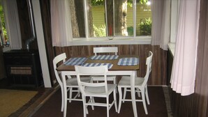 A dining area with a wooden table and white chairs, a window with curtains, and a wood-burning stove. - Bemus Point Vacation Rental (Bemus Point)