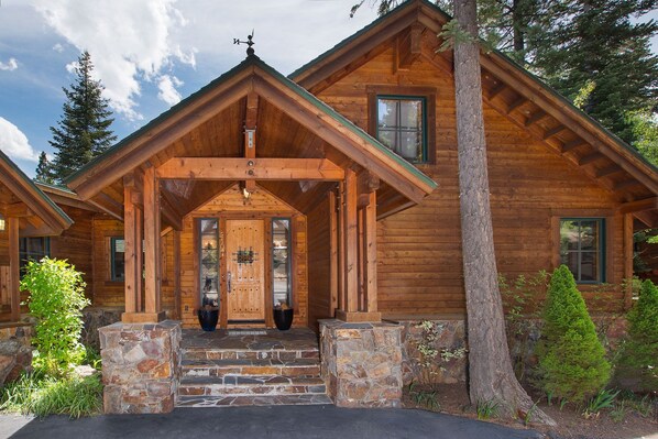 Une cabane en rondins avec des fondations en pierre, une véranda en bois et une grande porte d’entrée.