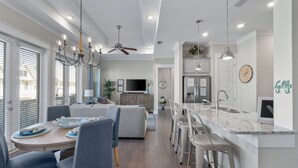 Eine moderne Küche mit Marmorarbeitsplatte, ein Essbereich mit rundem Tisch und ein Wohnzimmer mit Sofa und Fernseher.