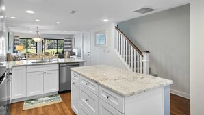 A modern kitchen with white cabinetry, granite countertops, and a central island. - 121 Greens-7 Min Walk to Beach, Full Remodel w/Beach Locker & Chairs (Hilton Head Island)