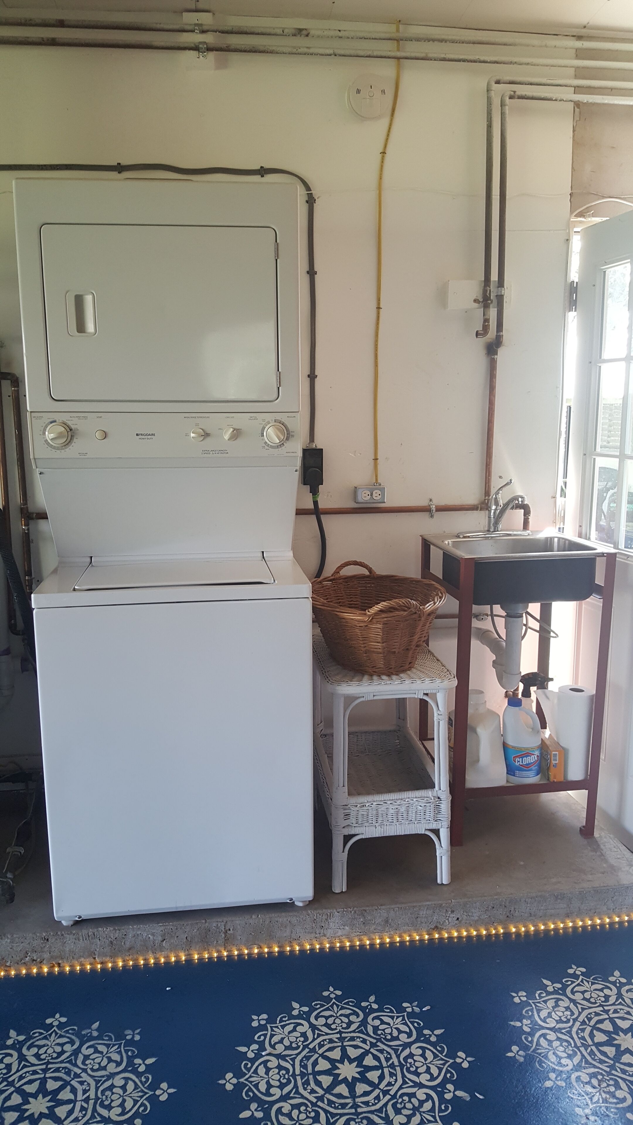 Un espace buanderie comprenant un lave-linge, un panier en osier, un évier et un sol à motifs.