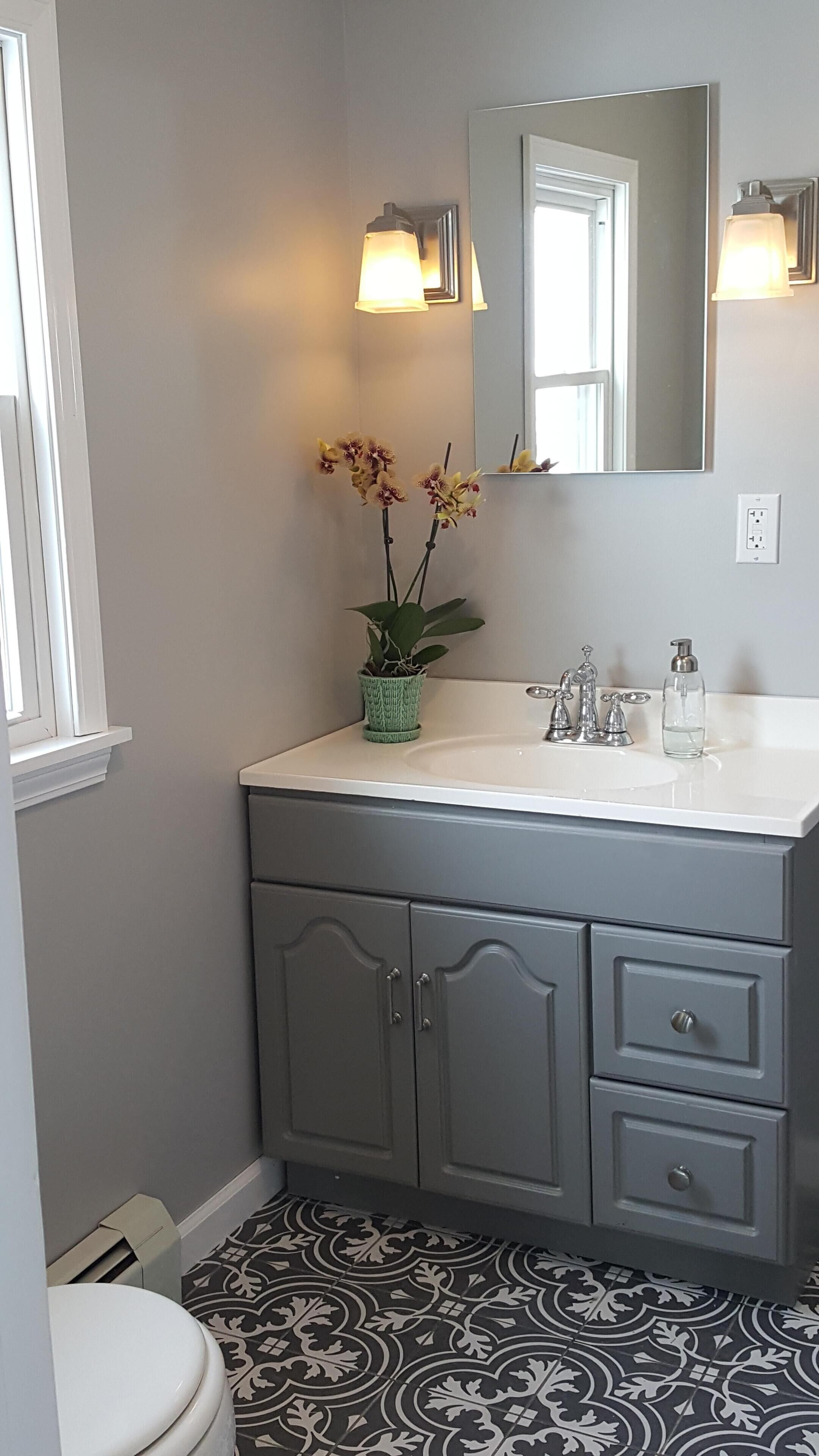 A bathroom with a white sink, two mirrors, a potted plant, and patterned floor tiles.