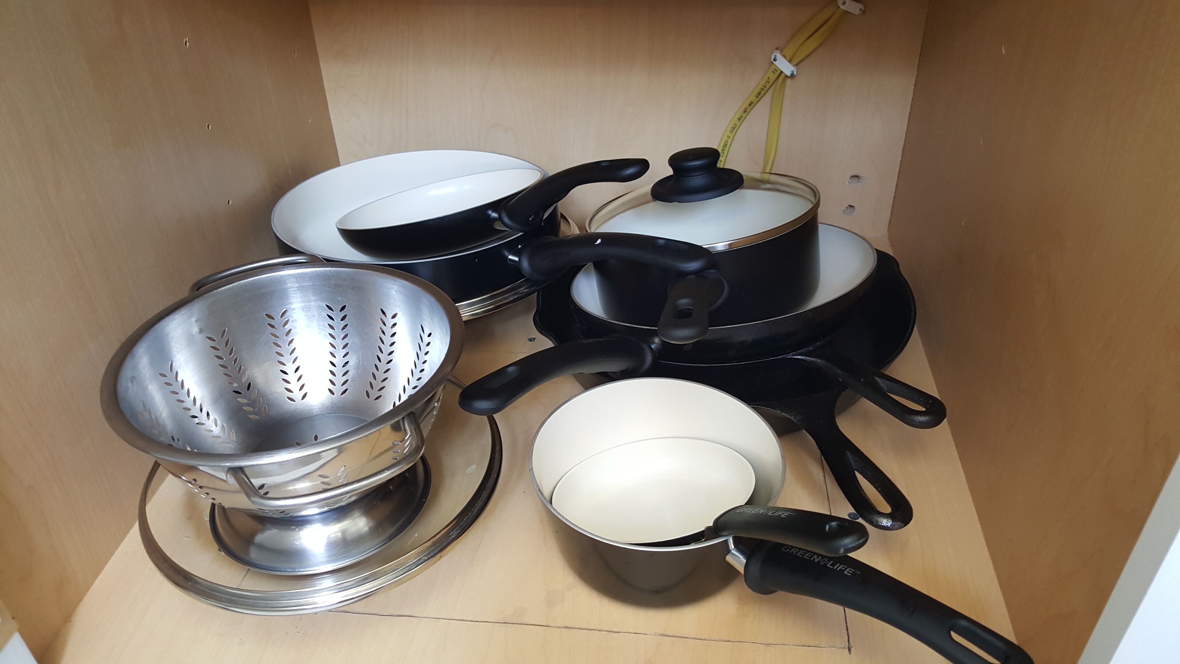 Uma cozinha com diversos utensílios de cozinha, incluindo panelas, frigideiras e um escorredor.