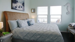 Ein Schlafzimmer mit einem großen Bett, einem Weidenkopfteil, einer Wanddekoration mit einem Seepferdchen und einem Gemälde von Booten an der Wand.