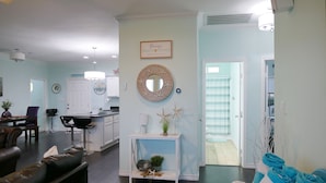 Ein Wohnzimmer mit einer dunkelbraunen Ledersofa, einem weißen Konsolentisch mit Dekoration und einer Küche im Hintergrund.