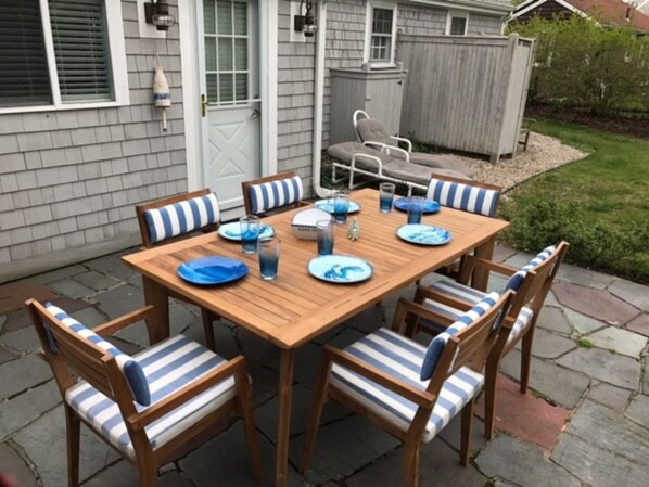 A wooden patio table with blue and white striped chairs, a small grill, and a dining set with plates and glasses.