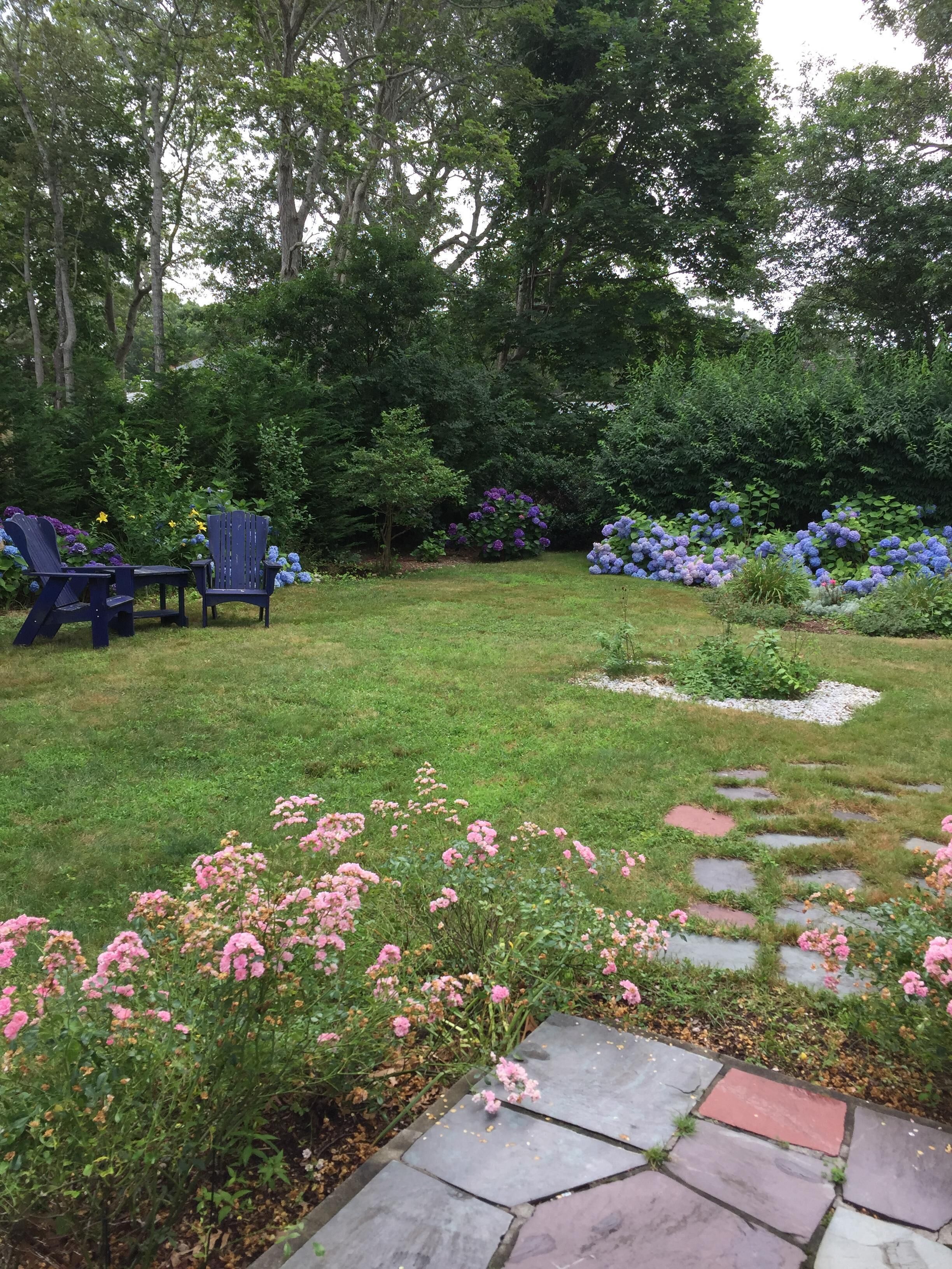 Un jardin avec une pelouse, un chemin en pierre et un espace aménagé avec des chaises.