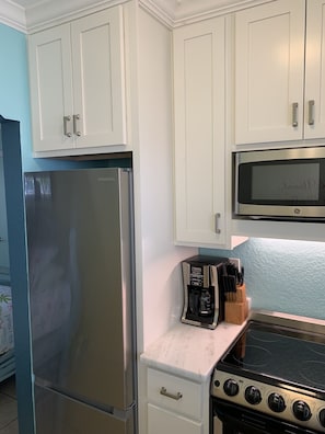 Compact kitchen area with a refrigerator, microwave, gas stove, and coffee maker.