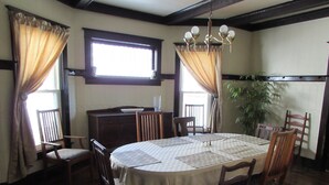 Ein Esszimmer mit einem runden Tisch, sechs Holzstühlen, einer Pendelleuchte, einer Topfpflanze und einem Fenster mit Vorhängen.