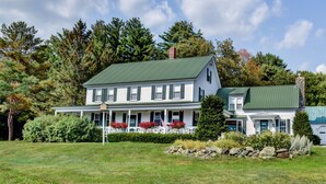 A two-story house with a green roof, a porch with white railings, and a stone wall in front. - Mountain House Magic (Newry)