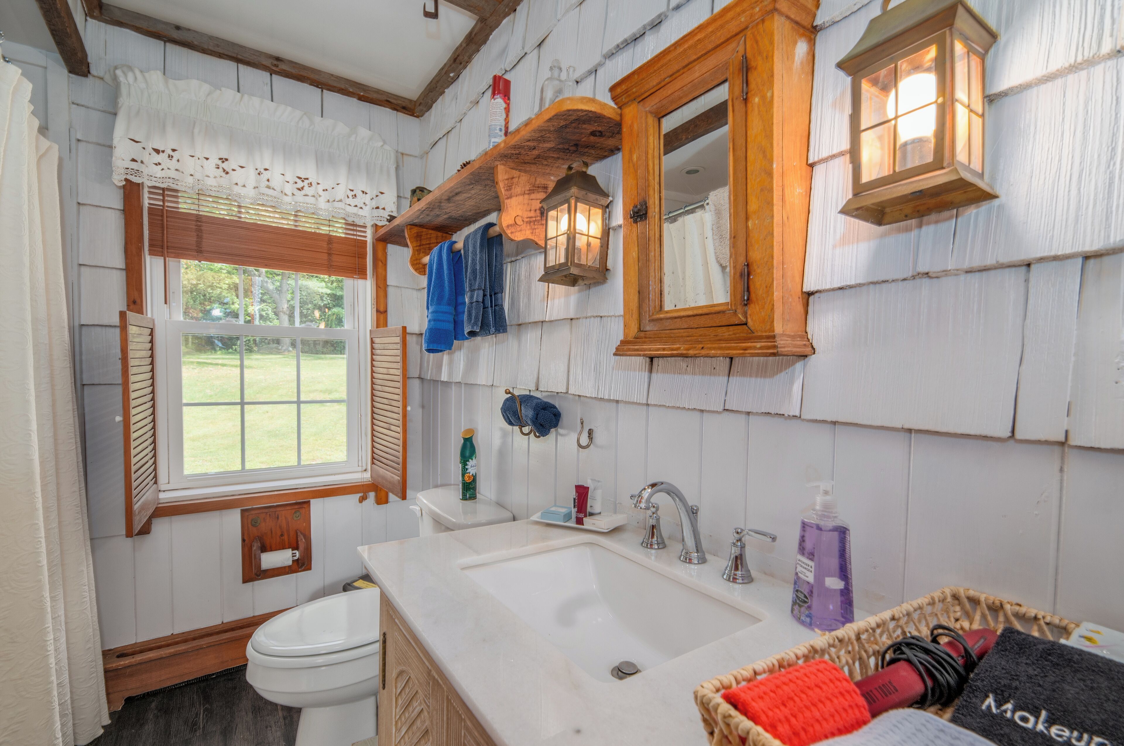 Une salle de bain avec un meuble-lavabo en bois, un évier, des toilettes et une fenêtre donnant sur l’extérieur.