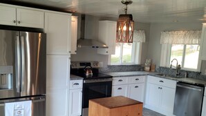 A modern kitchen with white cabinets, a stainless steel refrigerator, a wooden stool, and a stone-patterned floor. - Mountain House Magic (Newry)