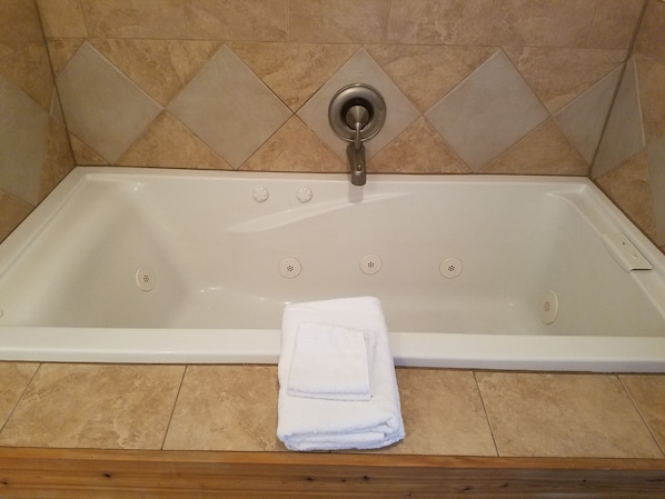 A white bathtub with a single faucet, a towel, and a wooden bath mat.